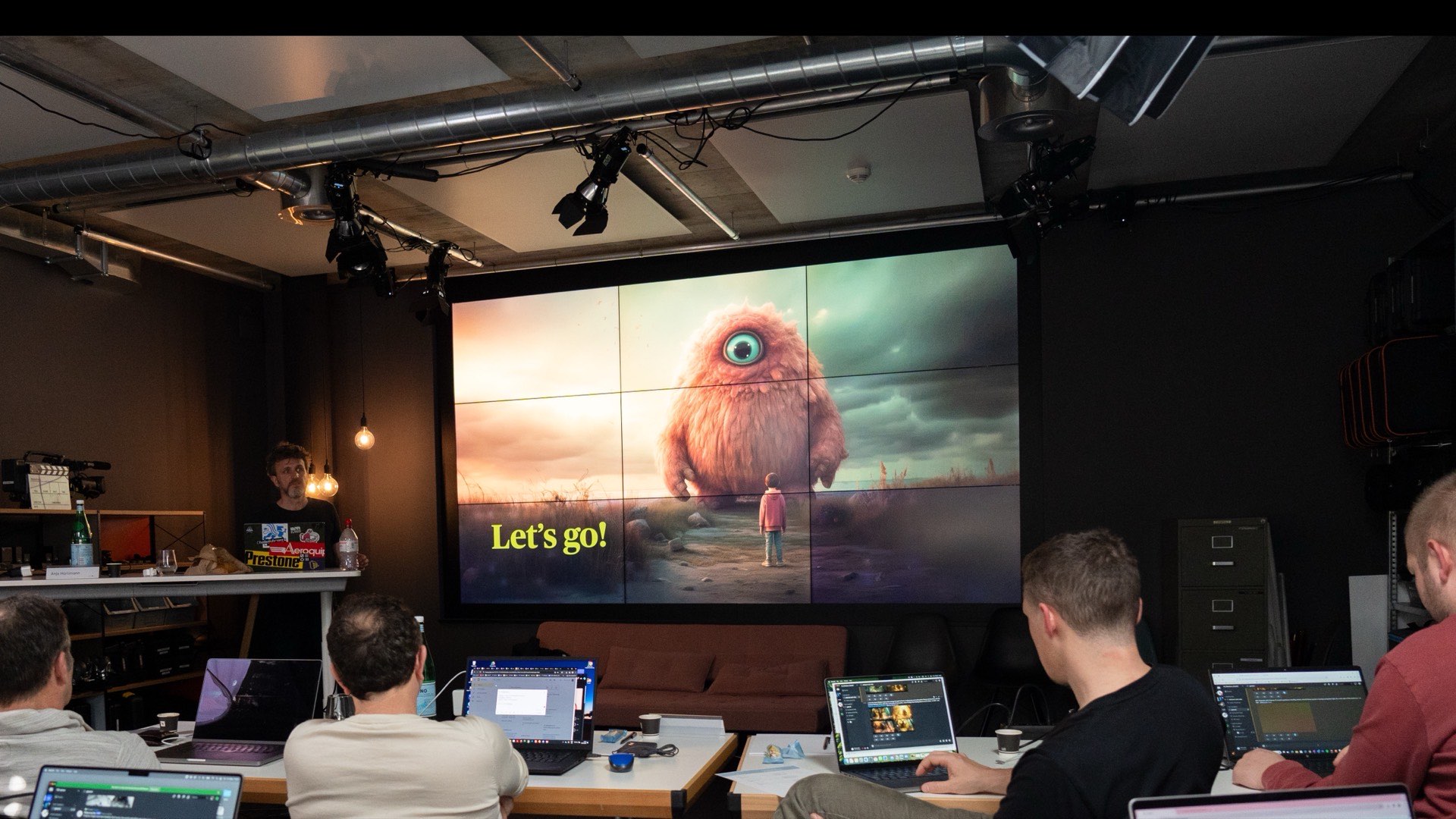 KI-Kurs bei Studio 1: Teilnehmende an Laptops vor der grossen Videowand mit einem KI-generierten Bild