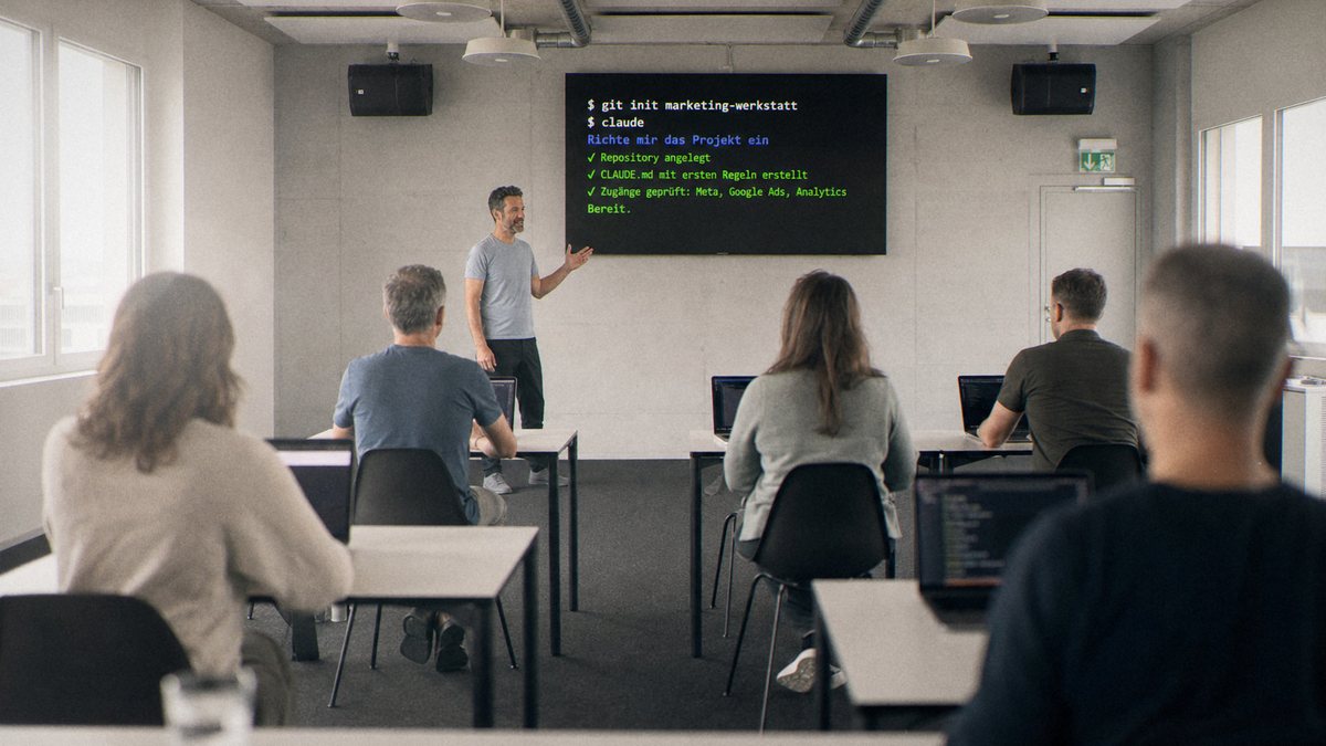 Teilnehmende richten am eigenen Laptop ihre KI-Werkstatt ein, auf der Videowand ein Terminal