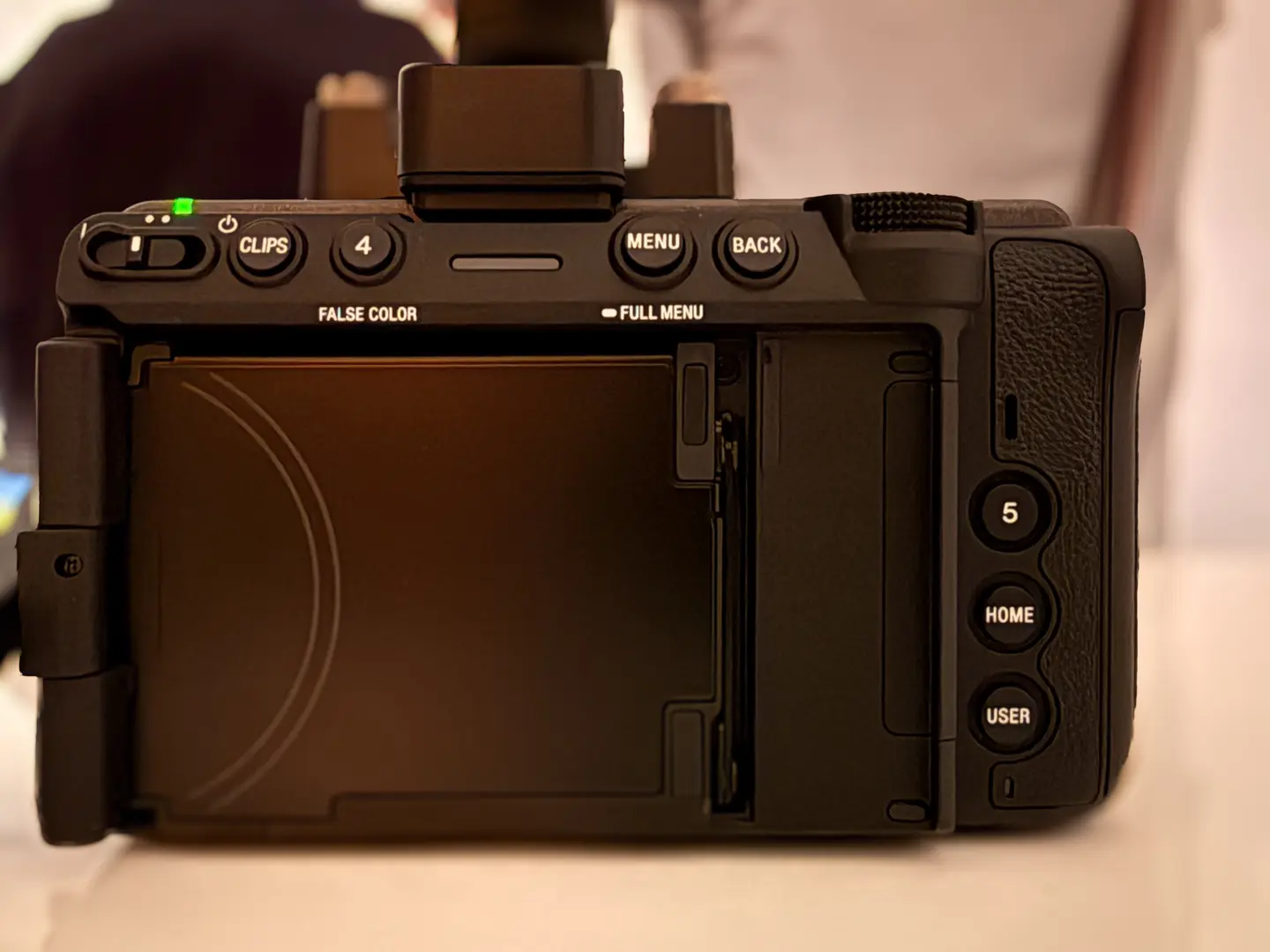 Rückseite einer Sony FX3 Videokamera mit ausklappbarem LCD-Touchscreen, Bedientasten (MENU, BACK, HOME, USER), Clips-Button und Nummer-4-Taste oben. Grüne LED leuchtet.