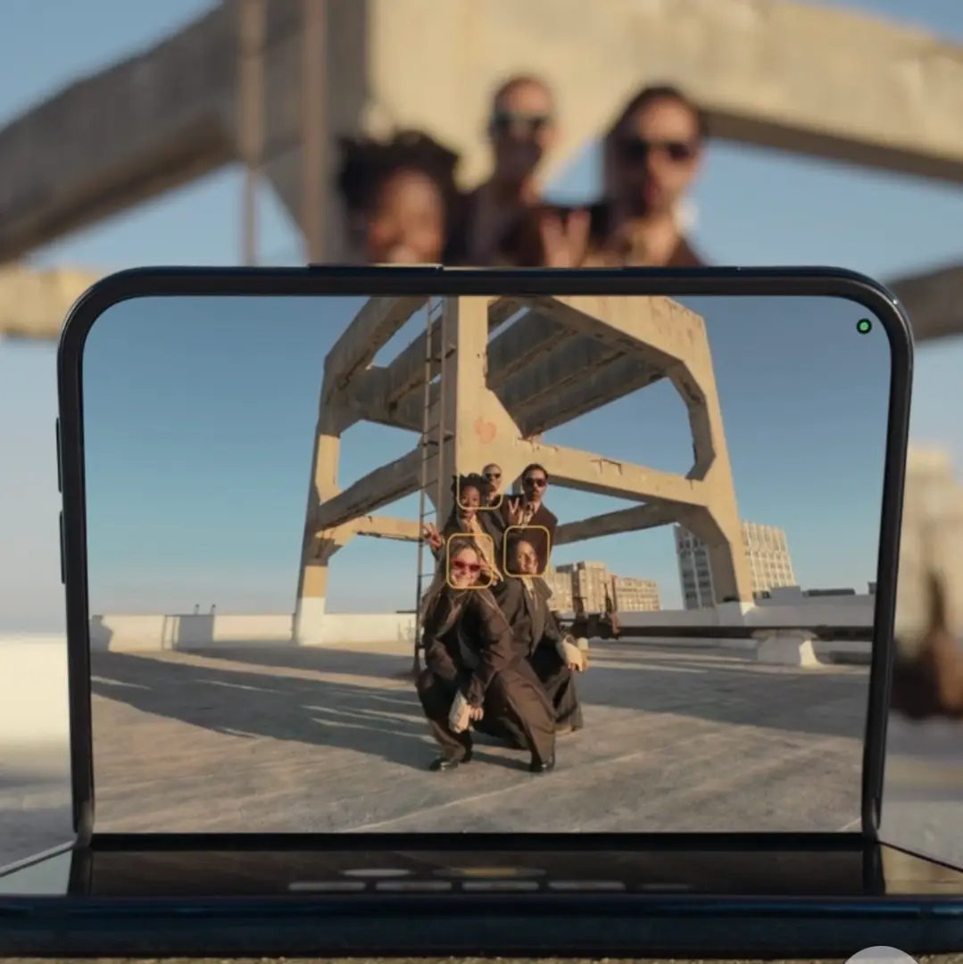 Aufgeklapptes iPhone Duo, das auf dem Innendisplay eine Gruppe von fünf Personen im Kamerabild zeigt, mit gelben Rahmen um die erkannten Gesichter.