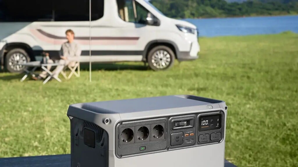DJI Power Auro 2000 Elite auf einem Tisch vor einem Camper am See. Sichtbar sind drei AC-Steckdosen, USB-Anschlüsse und ein D